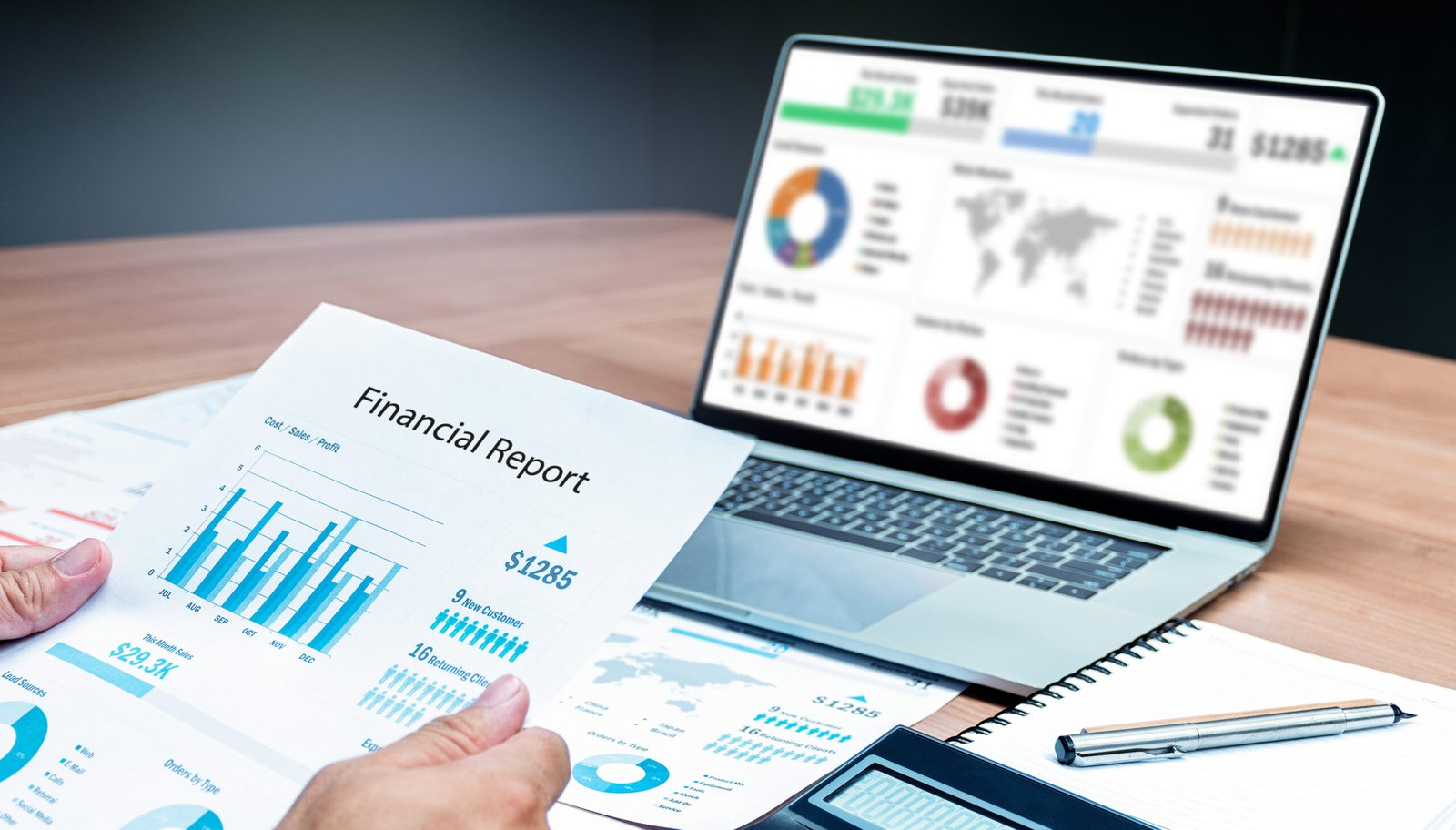 Businessman hand holding financial report document with mock up sales summary slide show presentation on display laptop and calculator ,notebook on table in meeting room
